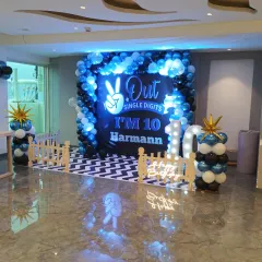 A stylish blue, black, and white balloon backdrop for a 10th birthday party. The setup includes marquee lights for the age and a custom floor print to complete the look.