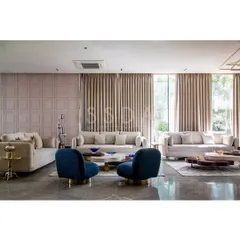 In the 'House Retold' project, the formal living room opens dramatically to the garden. The layout features multiple seating areas with plush sofas and bold blue accent chairs, creating a versatile space for conversation.