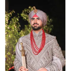 A classic portrait of a Sikh groom in his grey embroidered sherwani and red beaded necklace. His confident stance and the traditional kirpan create a powerful image.