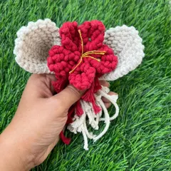 Holding a red macrame flower with cream-colored leaves. I love combining colors to create these unique floral elements for my nameplates and wall hangings.