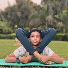 A young boy demonstrates a seated pose with his legs behind his head, showing incredible flexibility. We encourage kids to explore what their bodies can do in a safe and playful manner.