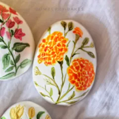 A close-up of a marzipan egg with a hand-painted marigold flower design.