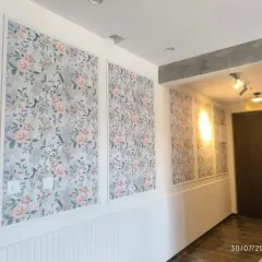 For this hallway, I used wainscoting to create vertical panels filled with a soft floral and bird-patterned wallpaper. This brightens the space and adds a classic, decorative touch.
