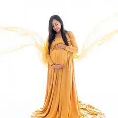 A graceful solo portrait featuring a flowing yellow maternity gown against a bright white backdrop. The soft fabric toss adds a touch of dynamic elegance to the shot.
