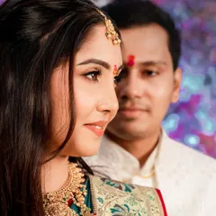 A close-up profile of the bride in her traditional attire, with the groom in the background. This artistic shot focuses on the bride's beauty and intricate jewelry.