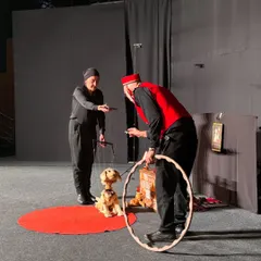 A scene from 'Pay Attention to Those Two', where a lazy dog puppet is encouraged to perform a trick. This Italian show uses classic marionette techniques to tell a heartwarming and funny story for all ages.