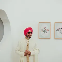 A cool and modern groom portrait. Dressed in a classic white sherwani and stylish sunglasses, he holds his kirpan, blending tradition with contemporary flair.
