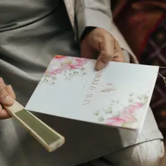 A guest holds the beautifully designed wedding program for Nikki & Avin, showing the elegant floral motif and custom monogram that was part of their wedding branding.