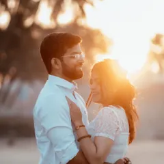 A close, romantic portrait of a couple bathed in the warm, soft light of the setting sun on a beach. The lens flare adds a touch of magic.