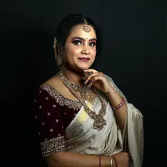 A studio portrait showcasing a bridal look with a modern twist. The makeup features a dramatic eye, while the off-white saree and maroon velvet blouse create a unique color combination.