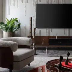 The custom wall paneling in the Scarlet Horizon living room serves as a textured backdrop for the media unit. This detail, combined with the plush boucle armchair and rich red marble coffee table, creates a space that is both dramatic and comfortable.