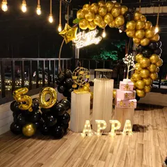 A stylish 50th birthday party for "Appa" on a terrace. The setup features a black and gold balloon ring, a personalized light-up name sign, and foil balloons marking the golden jubilee.