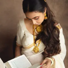 A quiet, contemplative moment. This close-up captures the intricate details of the traditional temple jewelry and the serene expression of the mom-to-be as she reads from a holy book.