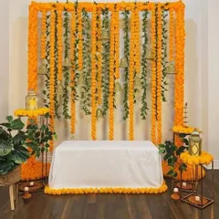 I created this indoor Haldi backdrop for a traditional home ceremony. It uses dense strings of bright orange marigolds accented with green leaves and hanging temple bells. The setup includes a clean, white-covered seat and matching floral arrangements on stands for a complete and authentic look.