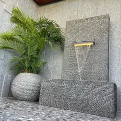 We also design and install custom water features as part of our landscaping services. This modern, freestanding fountain adds the soothing sound of water and acts as a focal point next to a potted palm.