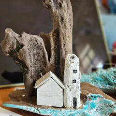 This is what my workbench looks like when a new driftwood collection is taking shape. Here, the blank canvases of the lighthouse and house are waiting for their details, sitting beside the raw, organic shape of the wood that will become their landscape.