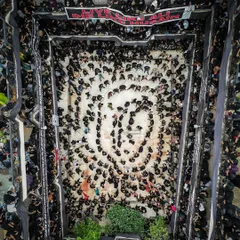 A wide, top-down aerial shot of a Muharram procession, showing participants forming a massive, swirling circle of devotion. This perspective reveals the scale and organized pattern of the ritual, which is impossible to see from the ground.