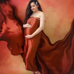 A moment of pure elegance. The rich, rust-colored satin fabric flows around the mother-to-be, creating a dramatic and artistic maternity portrait in the studio.