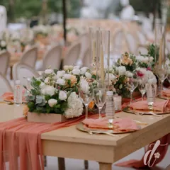 A close-up of a reception tablescape with a peach-colored runner, gold-rimmed charger plates, and a lush centerpiece of white and peach florals. Every element is coordinated to create a soft and romantic look.