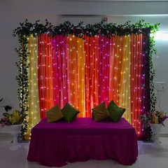 A simple and beautiful backdrop created with colorful drapes and fairy lights, perfect for home-based functions like Mehendi or a Chowki.