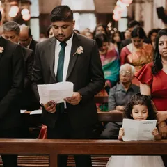 A young girl stands on a church pew, intently reading the ceremony leaflet alongside the adults. This charming photo captures a child's earnest attempt to participate in the grown-up world.