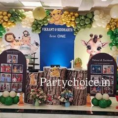 A cute jungle theme for a first birthday, featuring photo displays to celebrate the baby's first year. The setup includes a green and gold balloon arch, life-sized cutouts of Simba and Dumbo, and custom boards with monthly photos.
