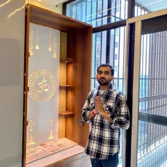 Standing with a completed mandir unit. This wooden design features a backlit acrylic panel with religious motifs and storage cabinets below.