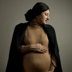 A classic and elegant maternity portrait. The simple, focused lighting highlights the beautiful silhouette of the baby bump, creating a timeless piece of art that you will cherish forever.