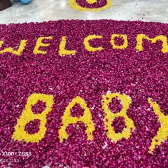 A close-up of the flower petal art, spelling out 'WELCOME BABY' with yellow marigolds on a bed of red rose petals.
