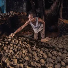 A potter carefully inspects a fresh batch of diyas, or clay lamps, before they are fired. The sheer volume of his craft fills the frame, showing the scale of production in this small workshop.