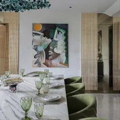 A closer look at the artful composition of the dining area. The abstract painting on the wall complements the green velvet chairs and the unique, sculptural chandelier made of green glass.