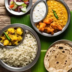 A simple, traditional meal served on a banana leaf for that authentic touch. This thali includes rice, aloo gobhi, a lentil dish, cooling raita, and soft chapatis, just like 'maa ke haath ka khana'.