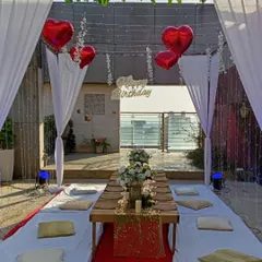 A romantic sit-down dinner setup on a terrace, perfect for a birthday or anniversary. This arrangement features low seating, a canopy with white drapes, and heart-shaped balloons for a celebratory touch.