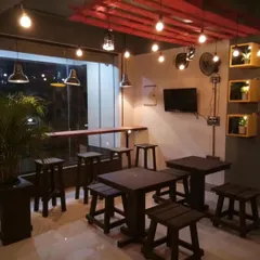 A cozy corner in a cafe we designed, featuring custom-built wooden tables and stools. The warm, industrial lighting and natural plant accents create a welcoming spot for customers.