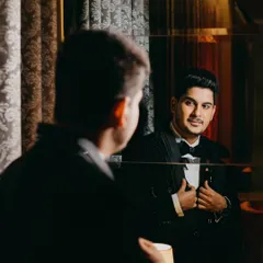 A confident groom checks his reflection before the reception. This candid yet stylish shot in his black tuxedo captures a moment of self-assurance and excitement.