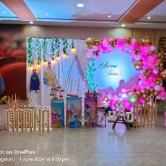 This Disney Princess party for Aarna's 4th birthday combines a curtain backdrop with a circular balloon arch. The setup includes princess cutouts, themed pedestals, and large marquee letters spelling "AARNA".