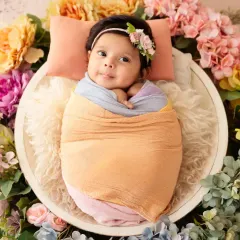 Capturing a beautiful, happy moment with this one-month-old baby girl. She is awake and smiling, wrapped in pastel colors and nestled in a basket encircled by a vibrant floral wreath.