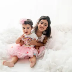 A perfect example of sibling love. The older sister holds her baby sister close in a dreamy setup of soft, white clouds, creating a truly angelic and sweet portrait.