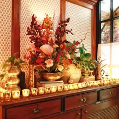 A close-up of a console table styled for a festive launch event. A large floral arrangement in warm, autumnal tones is surrounded by a sea of candles in mercury glass holders, creating a look of rustic elegance.