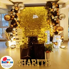 A chic and modern 15th birthday party. This setup uses a black and gold color scheme with a sequin wall, large marquee numbers, and geometric-patterned plinths.