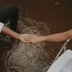 An artistic and symbolic shot of a couple holding hands while seated in chairs surrounded by water. This conceptual photo is about connection and trust.