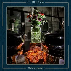 The interplay of light and decor is key to my setups. Here, fresh flowers in a simple glass vase are flanked by elegant copper and black chafing dishes, with the warm light from decorative candle holders creating a cozy and upscale feel.