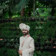 A full-length portrait of the groom standing confidently against a lush green background. His traditional attire and calm demeanor make for a very regal and handsome photograph.