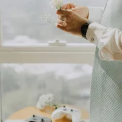 An artistic shot of the groom's hands holding delicate white flowers, with gaming controllers on the table. This unique detail shot perfectly blends romance with the couple's personal interests.