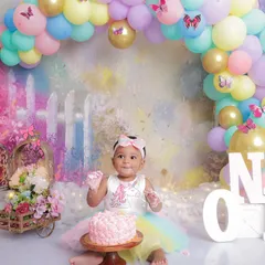 A sweet and slightly messy smile from the birthday girl. This photo captures the fun of a cake smash session, with a beautiful pastel garden backdrop and a colorful balloon arch.