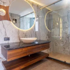 We created a spa-like retreat in this bathroom using floor-to-ceiling grey marble and warm, indirect lighting. The large, backlit circular mirror and floating wooden vanity enhance the sense of space and luxury, turning daily routines into a calming experience.