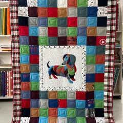Your memories, stitched with love. This custom T-shirt quilt features a colorful patchwork of treasured shirts, with a special appliqué of the family's beloved dachshund, making it a truly one-of-a-kind keepsake.