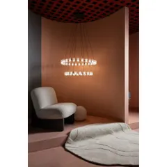 This cozy nook features a modern bouclé armchair and a tiered ring chandelier. We designed these spaces to feel like intimate living areas, helping customers visualize the lighting in their own homes.