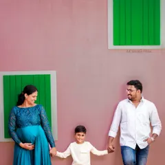 A fun and modern family portrait against a colorful studio wall. This shot captures the happy and relaxed dynamic of the family as they await their new addition.