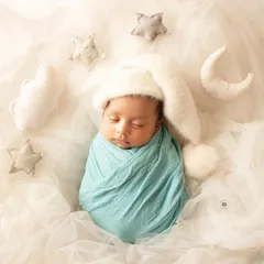 Dreaming on a cloud. This newborn is swaddled in blue and surrounded by soft, felted stars and a moon for a sweet celestial theme.